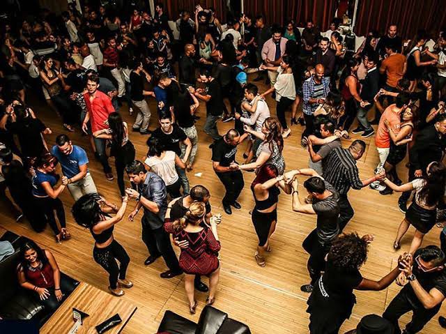 Many couples dancing salsa together on a crowded wooden dance floor.