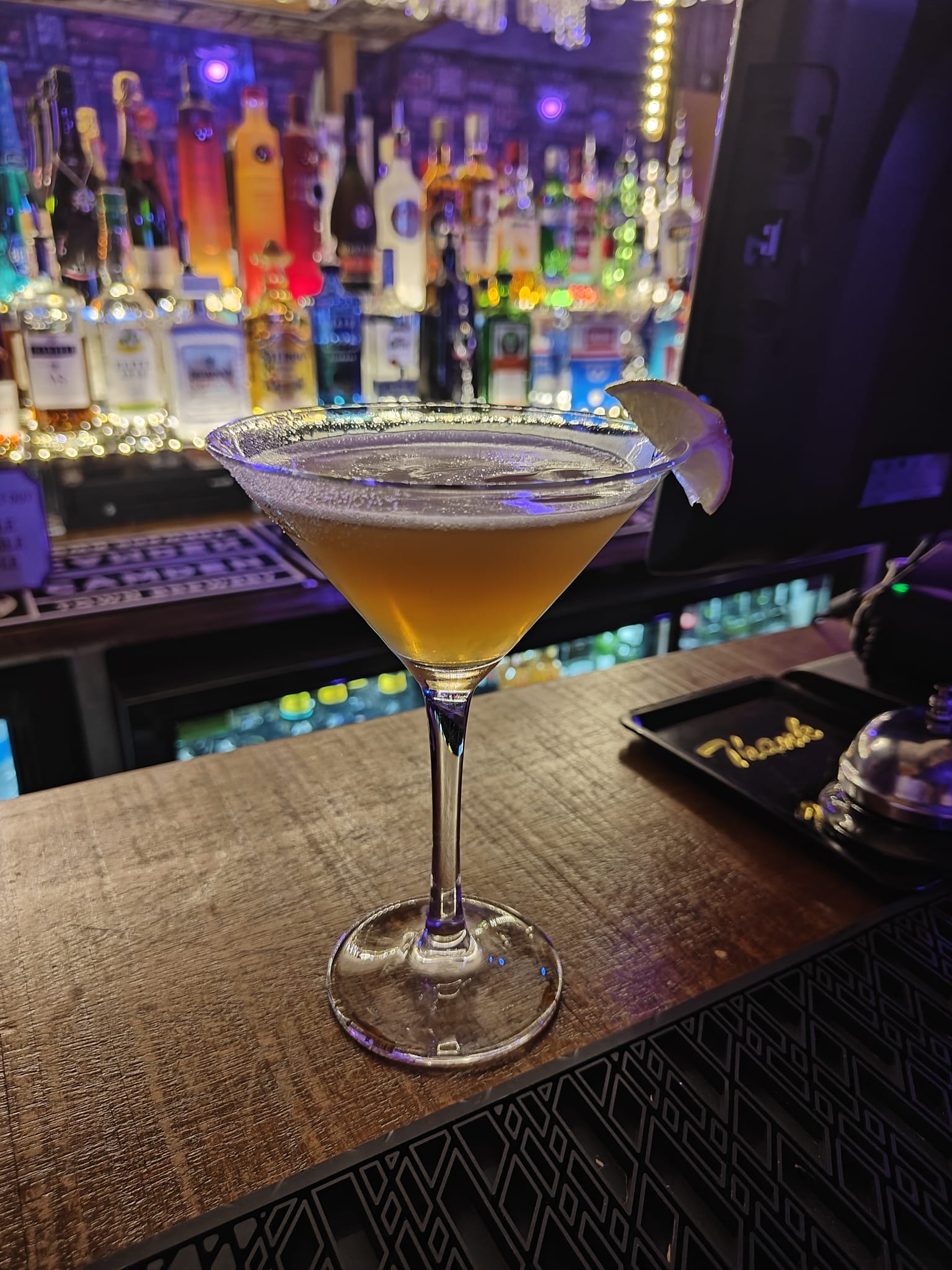 A signature cocktail on the bar top in front of the back-bar bottles.